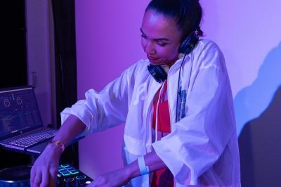 Une DJ mixant de la musique sur une console, dans un environnement éclairé par des lumières violettes.