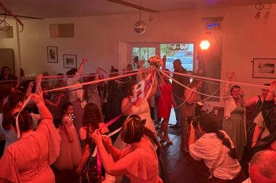 Des invités entourent une mariée avec des rubans colorés lors d'une célébration dans une salle éclairée.