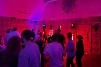 Des personnes dansent dans une salle éclairée par des lumières colorées, avec un mur décoré en arrière-plan.