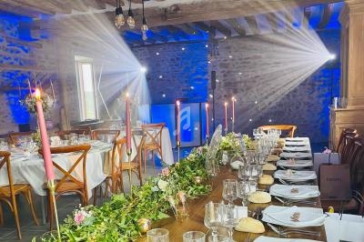 Salle de réception décorée pour un mariage avec tables dressées, bougies, guirlandes florales et éclairage tamisé.