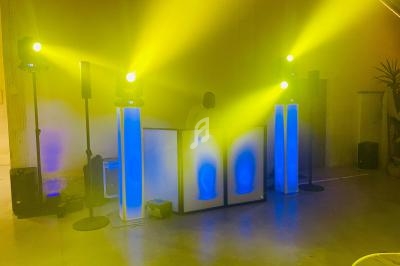 Installation de DJ avec éclairage jaune et bleu, comprenant des haut-parleurs et une table lumineuse dans une salle.