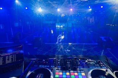 Vue d'une piste de danse vide éclairée par des lumières colorées, avec une table de mixage en premier plan.