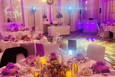 Salle de réception élégante avec tables décorées de fleurs violettes, bougies et éclairage tamisé.