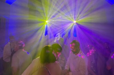 Personnes dansant sous des lumières colorées et des faisceaux lumineux dans une ambiance festive.