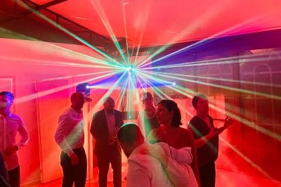 Des personnes dansent sous des lumières colorées et des effets laser dans une ambiance festive en intérieur.