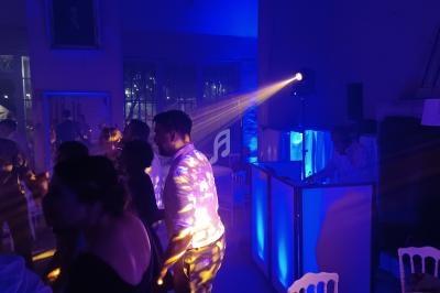 Des personnes dansent sous des éclairages colorés dans une ambiance festive avec un DJ en arrière-plan.