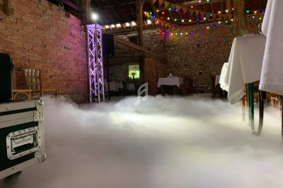 Salle en briques avec tables dressées, éclairage coloré et sol couvert de fumée artificielle.