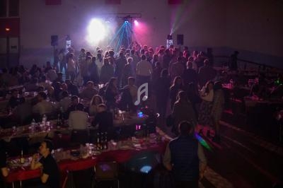 Salle remplie de convives assis et debout, éclairée par des lumières colorées et une ambiance festive.