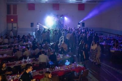 Salle de réception avec des tables dressées et des invités dansant sous des jeux de lumière sur une scène.