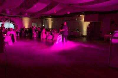 Un couple danse au centre d'une salle de réception éclairée par des lumières roses, entouré d'invités assis.