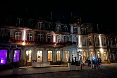 Façade d'un bâtiment historique éclairé la nuit, avec des lumières colorées et un petit groupe de personnes devant.