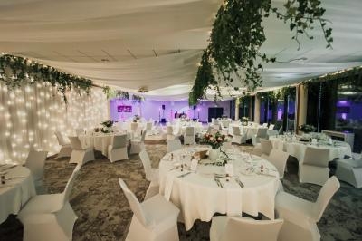 Salle de réception décorée avec des guirlandes lumineuses, des nappes blanches et des arrangements floraux sur les tables.