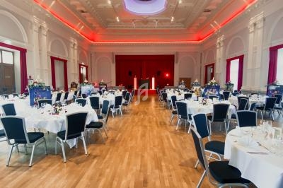 Salle de réception élégante avec parquet, tables dressées et éclairage rouge au plafond.