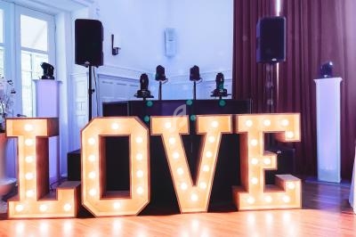 Lettres lumineuses formant le mot ’LOVE’ devant une installation sonore dans une salle éclairée.