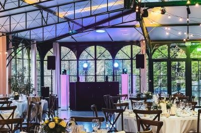 Salle de réception lumineuse avec tables dressées, chaises en bois et une piste de danse équipée de lumières colorées.