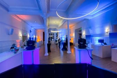 Salle de réception moderne avec éclairage coloré, colonnes blanches et tables disposées pour un événement.