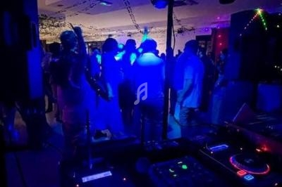 Vue d'une piste de danse éclairée par des lumières colorées, avec une table de mixage au premier plan.