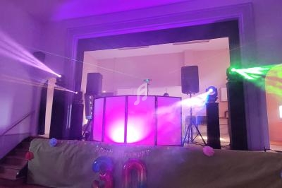 Scène décorée avec éclairages colorés, projecteurs et table de mixage sur une estrade dans une salle de fête.