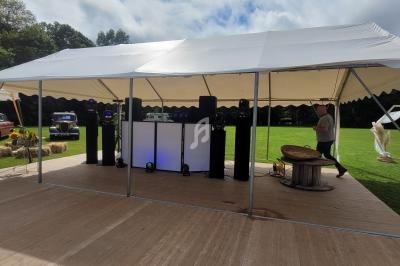 Structure en toile blanche montée sur une plateforme en bois, avec équipement audio et éclairage, dans un espace extérieur.