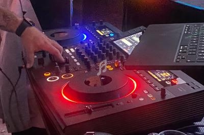 Main ajustant les commandes d'une table de mixage DJ avec des lumières colorées et un ordinateur portable à proximité.