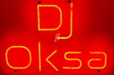 Enseigne lumineuse rouge et jaune avec l'inscription ’DJ Oksa’ en lettres néon.