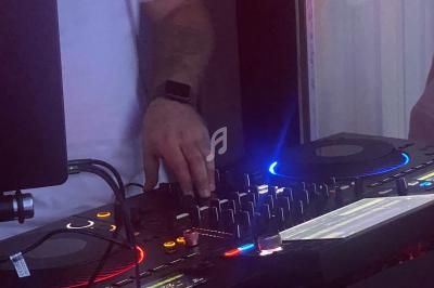 Un DJ mixant sur une table de mixage lumineuse avec des boutons éclairés dans une pièce faiblement éclairée.