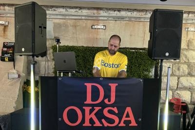 Un DJ mixant derrière une table équipée de haut-parleurs et d'une bannière avec ses coordonnées.