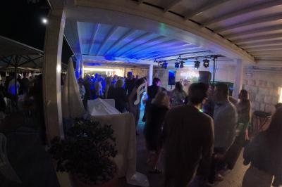 Groupe de personnes dansant et discutant sous une terrasse éclairée par des lumières colorées en soirée.