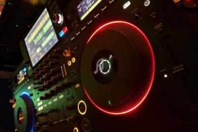 Platines DJ avec écrans, boutons et anneaux lumineux rouges et bleus dans un environnement sombre.