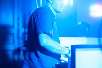 Un homme debout, éclairé par une lumière bleue, utilise un équipement électronique dans un environnement sombre.