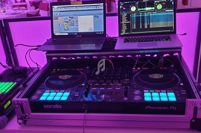 Équipement de DJ avec deux ordinateurs portables, une table de mixage et des platines, éclairé par une lumière violette.