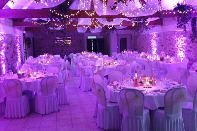 Salle de réception décorée avec des tables rondes, nappes blanches, éclairage violet et guirlandes lumineuses suspendues.