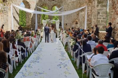 Cérémonie de mariage en plein air dans une ancienne ruine, avec des invités assis et un couple devant l'autel.