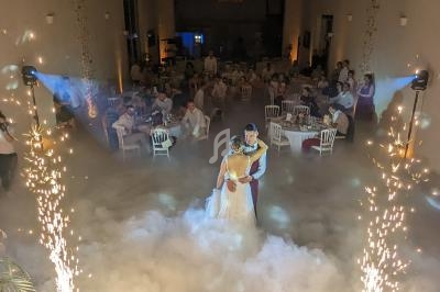Un couple danse au centre d'une salle de réception décorée, entouré de fumée et d'effets pyrotechniques.