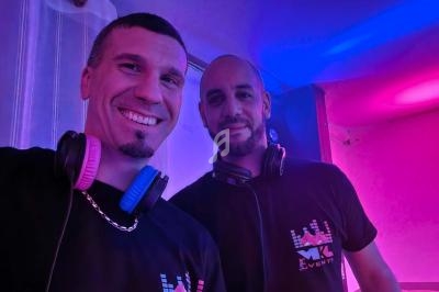Deux hommes souriants portant des casques audio autour du cou, éclairés par des lumières colorées dans un environnement…