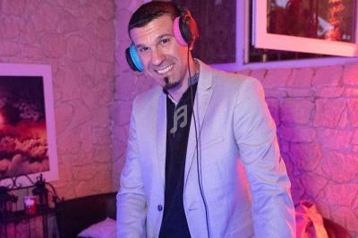 Homme souriant portant un casque audio, debout dans un environnement intérieur éclairé par des lumières colorées.