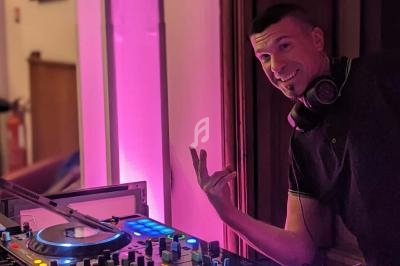 Un DJ souriant mixe de la musique sur une table de mixage éclairée par une lumière rose.