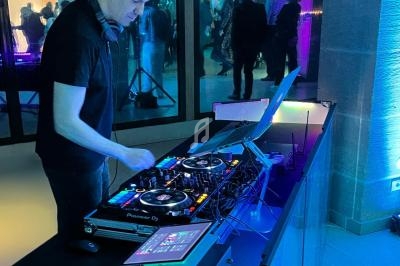 Un DJ mixe de la musique sur une table de mixage dans un espace éclairé par des lumières colorées.