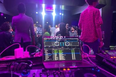 Vue depuis une table de mixage avec un écran affichant des pistes audio, face à une foule dans une salle éclairée.