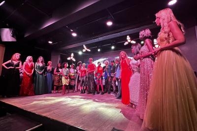 Un groupe de personnes en tenue de soirée est rassemblé sur une scène éclairée dans une salle sombre.