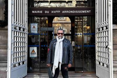 Homme debout devant l'entrée de la mairie du 16e arrondissement de Paris, avec des grilles ouvertes et une façade vitrée.