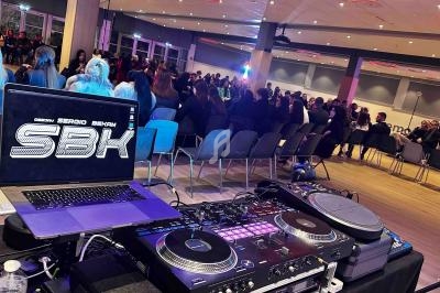 Vue d'une salle de conférence avec un DJ installé au premier plan et un public assis en arrière-plan.