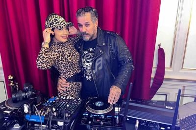 Une femme en tenue léopard et un homme en veste en cuir posent derrière une table de mixage avec des platines DJ.