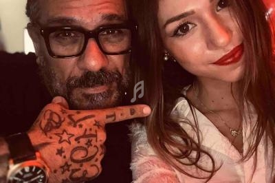 Un homme barbu avec des lunettes et des tatouages pose à côté d'une femme souriante dans un éclairage rouge tamisé.