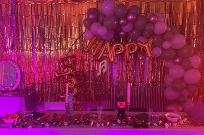 Décoration festive avec ballons, guirlandes dorées et table dressée contenant boissons, bougies et collations.