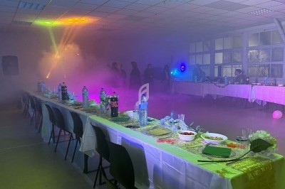 Salle décorée pour un événement avec tables dressées, éclairages colorés et ambiance enfumée.