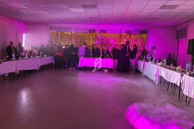 Salle décorée pour une fête avec des invités debout près d'une table, éclairage violet et fumée au sol.