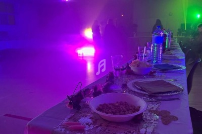 Table dressée avec des plats et boissons au premier plan, éclairage coloré et silhouettes de personnes en arrière-plan.