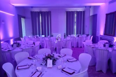 Salle de réception décorée avec des tables rondes dressées, nappes blanches et éclairage violet tamisé.