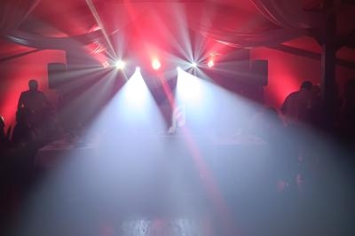 Salle de réception avec éclairage rouge et projecteurs lumineux diffusant de la fumée sur une piste en bois.